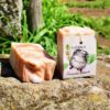 Savon artisanal La Masca au patchouli, posé sur une pierre en extérieur avec une étiquette illustrée d’un chaudron et de feuilles vertes. Savon marbré aux tons orangés et blancs.