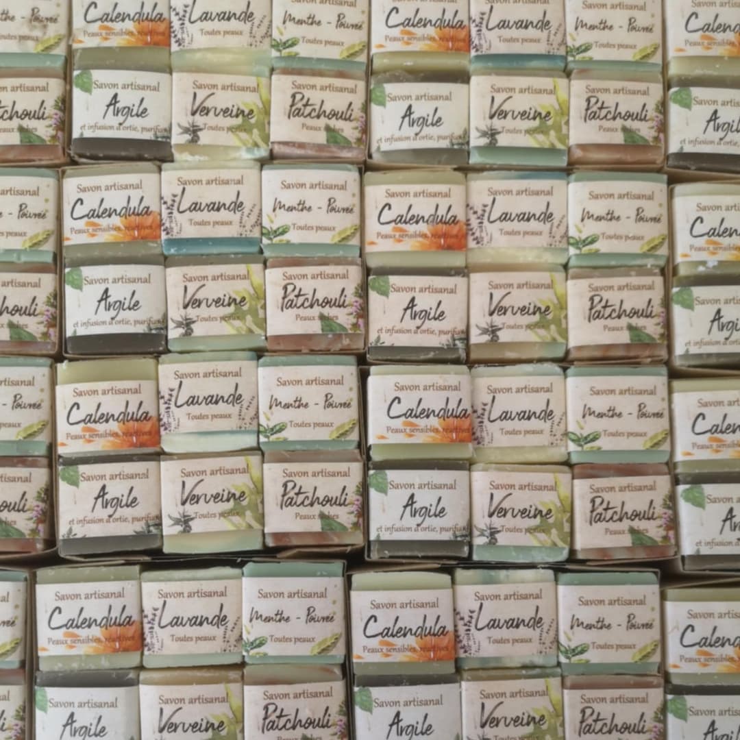 Ensemble de savons artisanaux La Masca emballés, alignés en rangées. Variétés visibles : Lavande, Patchouli, Verveine, Calendula, Argile, Menthe-Pinède. Savons naturels pour tous types de peau, fabriqués à base d'ingrédients végétaux.