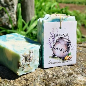 Savon artisanal La Masca à la lavande, posé sur une pierre en extérieur avec une étiquette illustrée d’un chaudron et de fleurs de lavande. Savon marbré bleu et vert avec fleurs de lavande séchées.